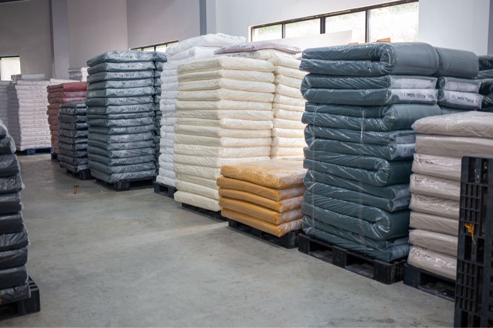 Wrapped fabric rolls in grey, cream and teal stacked high on pallets in the fabric store.