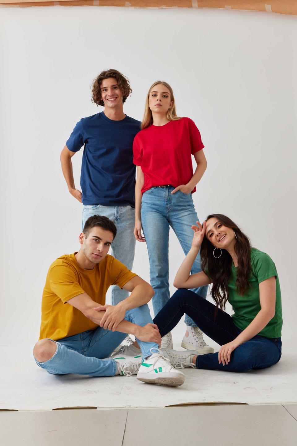 Four models in plain tees in navy, red, mustard and green, posed together in a white studio.