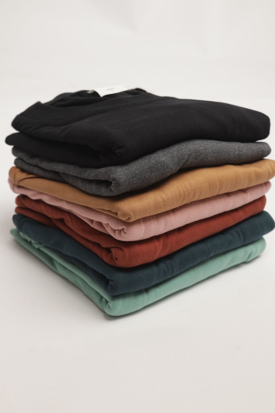 A neat stack of folded tees in black, charcoal, tan, peach, rust, teal and mint.