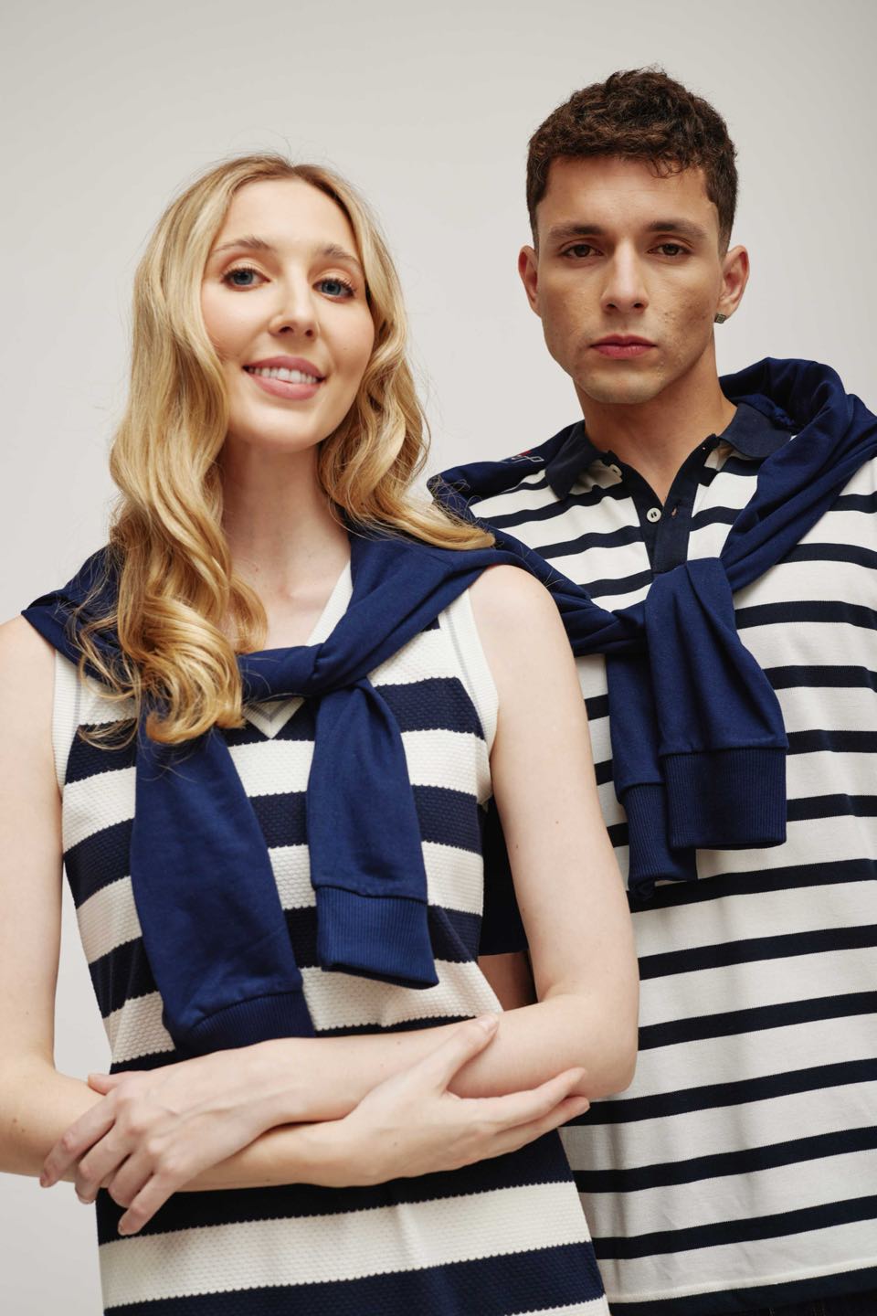 A woman and a man in navy-and-white striped knit tops, with navy sweaters knotted over their shoulders.